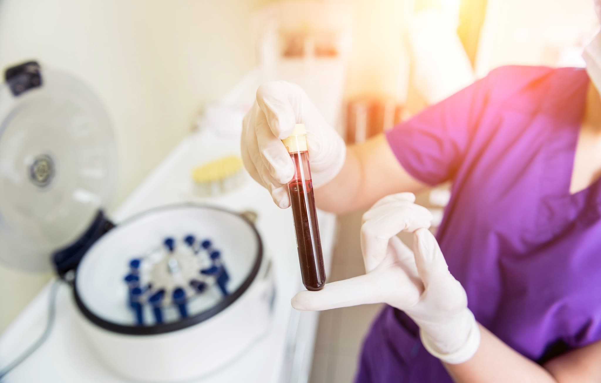 Gloved hands holding a sample tube beside a laboratory centrifuge
